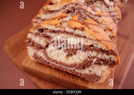 primo piano di torta in marmo affettata con ricchi vortici di vaniglia e cioccolato su un tagliere in legno con fondo morbido, morbidezza, brownie, yumm Foto Stock