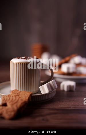 accogliente caffè con cappuccino con schiuma, biscotti e marshmallow su un tavolo di legno, che evocano un'atmosfera calda e invitante in autunno, un ambiente sereno, Foto Stock