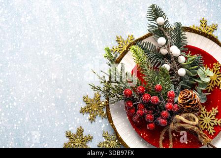 Cena di Natale. Vista dall'alto dei rami di bacche rosse di natale su un piatto rosso e spazio per testo su uno sfondo con fiocchi di neve. Conc. Natale Foto Stock