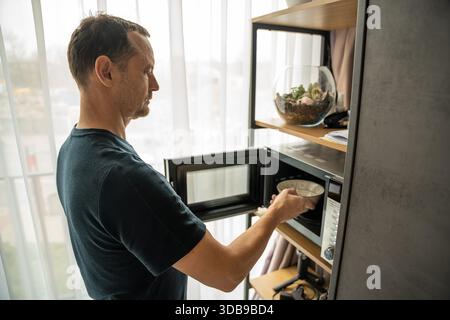 Uomo che usa un forno a microonde in una cucina di casa. Preparazione quotidiana del cibo. Foto Stock