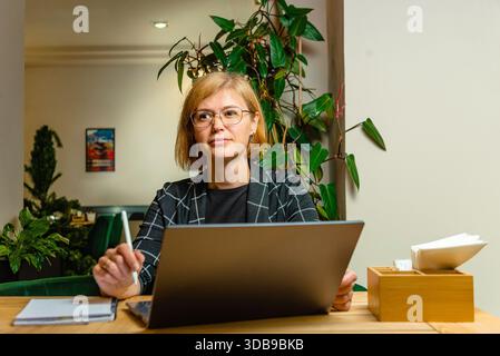 Una donna con gli occhiali indossa il proprio laptop mentre si gode un ambiente rilassato. Foto Stock