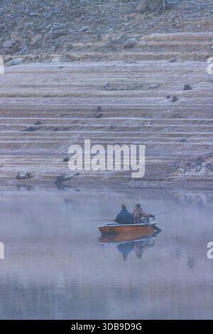 Due uomini che pescano da una piccola barca su un bacino nebbioso durante una fredda giornata invernale Foto Stock