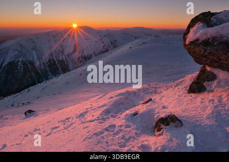 Veduta aerea del sole che splende sulle cime innevate di Derese nei Low Tatra, bagnate dal caldo bagliore dell'alba, dai Low Tatra, dalla regione di Zilina, Foto Stock