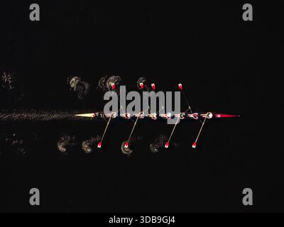 Vista aerea di una squadra di canottaggio che affetta le acque scure, i remi che creano motivi vorticosi, Boston, Massachusetts, Stati Uniti. Foto Stock