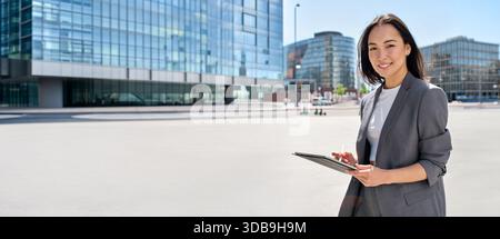 Giovane donna d'affari asiatica felice in piedi sulla strada della città con un tablet digitale. Foto Stock