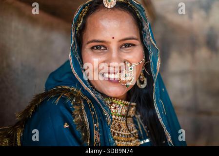 Sposa indiana sorridente che indossa abiti tradizionali e gioielli ornati, ritratto in luce naturale. Foto Stock