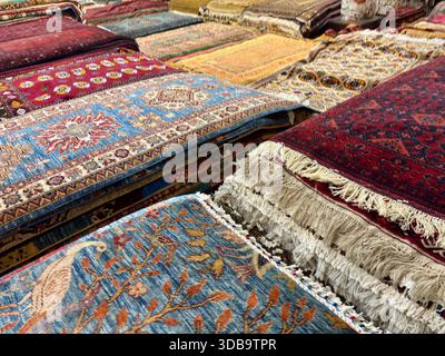 Tappeti e tappeti tradizionali dell'Asia centrale riccamente colorati accatastati in vendita Foto Stock