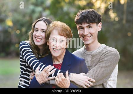 Nonna felice abbracciata da due giovani adulti sorridenti all'aperto. Foto Stock