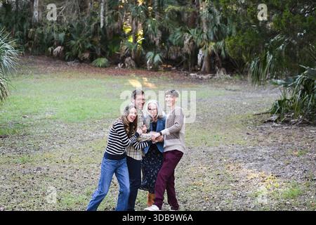 Gruppo di quattro persone che ridono e tengono per mano in una radura forestale. Foto Stock