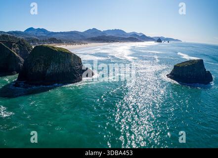 Vista aerea delle aspre scogliere che incontrano il mare turchese, le onde si schiantano contro la riva e le montagne si insinuano in lontananza, Oregon Coast, Oregon, Stati Uniti Foto Stock