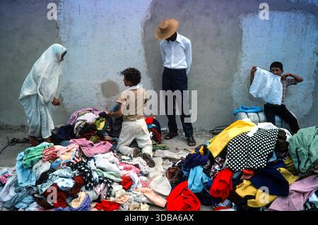I vecchi tessuti per la rivendita di moda veloce del Nord del mondo sono venduti ai paesi del terzo mondo negli anni '1970 del Nord Africa. Donna e figli che raccolgono una grande pila di vestiti di seconda mano indesiderati. Commerciante di mercato che li controlla. Kairouan, Tunisia, Nord Africa anni '1976 1970 HOMER SYKES Foto Stock