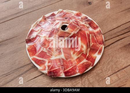 Una fotografia che enfatizza la consistenza setosa e il ​​color rubino profondo di un prosciutto alimentato a ghiande, servito su una base di pane rustico. Foto Stock