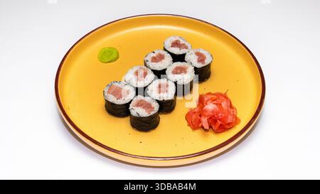 Tradizionali involtini di sushi hosomaki di tonno serviti con wasabi e zenzero sottaceto su piatto di ceramica gialla isolato su sfondo bianco. Foto Stock
