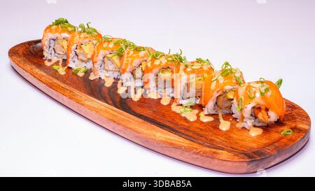 Sushi all'uramaki Fusion con salmone, tempura di gamberi e salsa cremosa serviti su una tavola di legno isolata su sfondo bianco. Foto Stock
