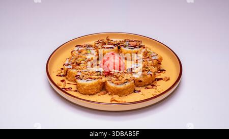 Sushi panini fritti con cipolle croccanti e salsa serviti su un piatto di ceramica gialla isolato su sfondo bianco. Foto Stock