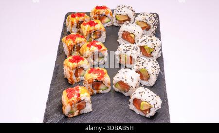 Set di sushi con involtini uramaki di salmone e avocado ricoperti di semi di sesamo e involtini premium con salsa e tobiko rosso su tavola. Foto Stock