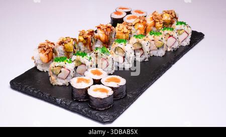 Piatto di sushi assortito di prima qualità con vari sushi roll e maki serviti su una tavola di ardesia nera isolata su sfondo bianco. Foto Stock
