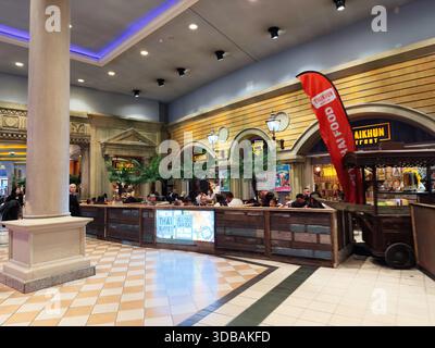 Stretford, Regno Unito - 15 novembre 2025: Affollata zona pranzo di Thaikhun all'interno di un centro commerciale di Manchester con palme, illuminazione calda e bancarelle di cibo. Foto Stock
