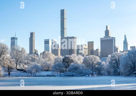 Scena invernale di New York City a Central Park con lago ghiacciato e alberi innevati, grattacieli di Midtown Manhattan che si innalzano sullo sfondo Foto Stock