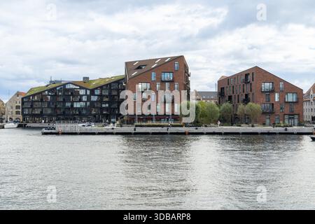 Copenaghen, Danimarca - 30 settembre 2025: Vista dei moderni edifici in mattoni con tetti verdi che si riflettono nelle calme acque del canale sotto un cielo nuvoloso. Foto Stock
