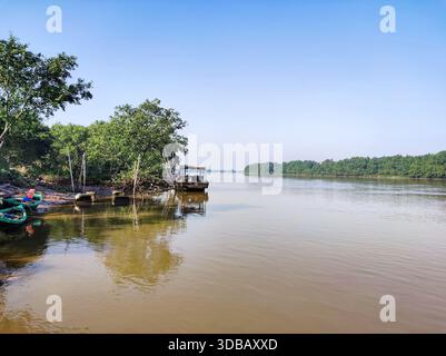 Tranquilla scena tropicale del fiume con piccole barche da pesca attraccate da una verdeggiante foresta di mangrovie in una giornata di sole nel sud-est asiatico. Foto Stock
