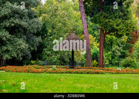 un pittoresco giardino caratterizzato da un tetto di paglia riparato tra vegetazione lussureggiante e vivaci aiuole di fiori Foto Stock