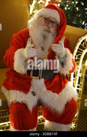 Uomo vestito da Babbo Natale che regala due pollici in un ambiente natalizio con luci e decorazioni.Nantes, Francia Foto Stock