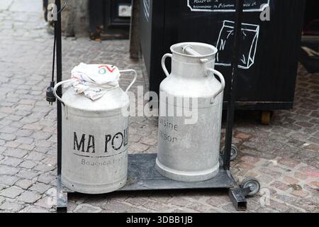 Due lattine di latte vintage in metallo esposte su uno stand con ruote all'esterno in una strada acciottolata. Nantes, Francia Foto Stock