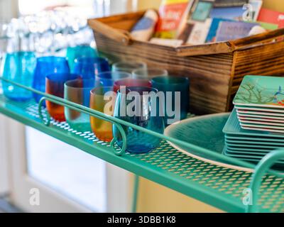 Primo piano di bicchieri da vino, piatti e un cestino di libri su uno scaffale. Foto Stock