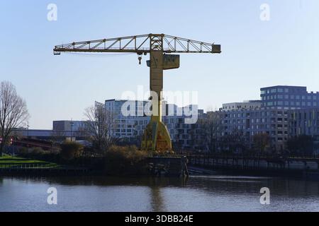 Un'alta gru industriale gialla si trova accanto al fiume con moderni edifici di appartamenti sullo sfondo. Nantes, Francia Foto Stock