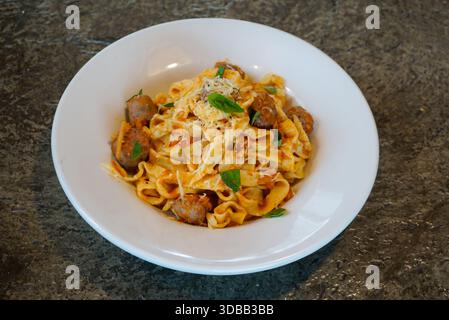 Tagliatelle di pasta con salsiccia in salsa di pomodoro condite con parmigiano e basilico fresco, servite in ciotola bianca, cucina italiana. Foto Stock