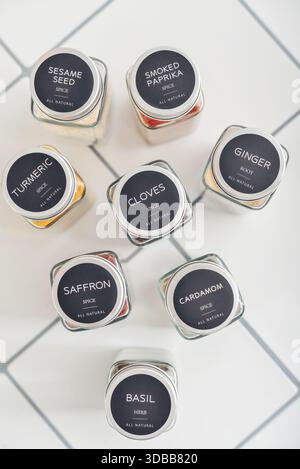 Spezie assortite in vasetti di vetro con coperchi in metallo sul piano della cucina piastrellato Foto Stock