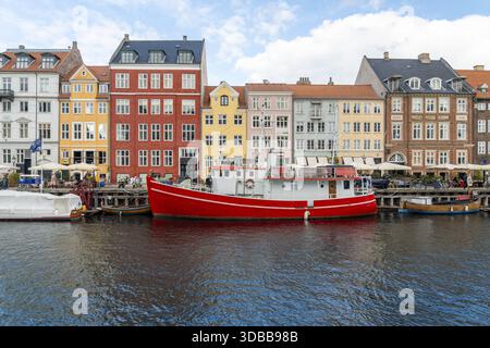 Vista di edifici vivaci e colorati che si riflettono nelle tranquille acque accanto a una suggestiva barca rossa nel porto di Nyhavn, Copenaghen, Danimarca. Foto Stock