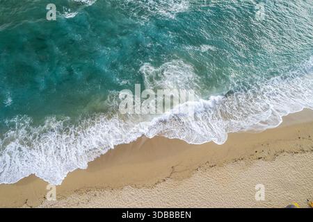 Vista aerea delle acque turchesi che si infrangono tra le onde bianche spumeggianti contro le sabbie baciate dal sole della costa, creando un incredibile contrasto di colore e tessuto Foto Stock