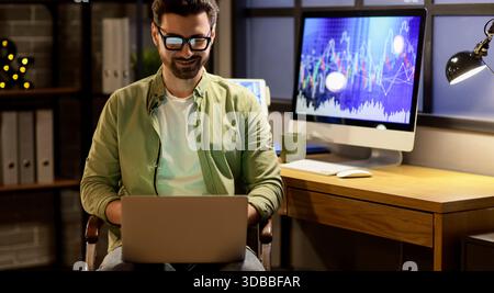 Commerciante di sesso maschile che lavora su un laptop in ufficio di notte Foto Stock