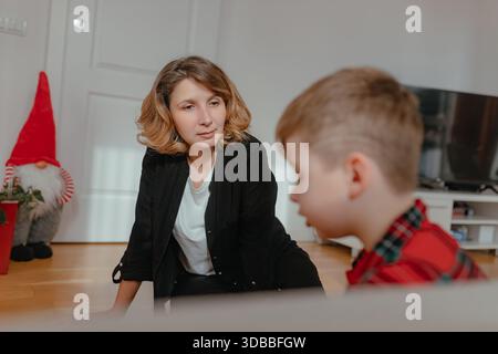 Donna che osserva i bambini seduti sul pavimento interno della casa pigiama rosso chiaro e soffice stanza in legno ambiente tranquillo per i genitori. Foto Stock
