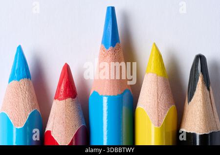 Primo piano delle punte affilate di cinque matite colorate blu, rosso, giallo, nero con venature di legno visibili e piombo, disposte in fila, su sfondo bianco. Foto Stock