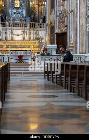 solenne momento di preghiera all'interno di una chiesa italiana riccamente decorata, concentrandosi sul pavimento piastrellato, sulle pere di legno vuote e su un adoratore solitario vicino a t Foto Stock