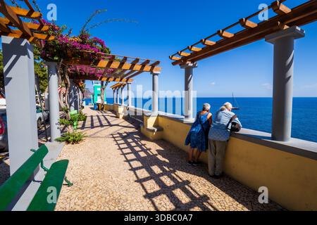 Splendida vista di una coppia di anziani appoggiata sulla banister e godendo della vista sopraelevata dell'Oceano Atlantico da Funchal a Madeira, in Portogallo Foto Stock