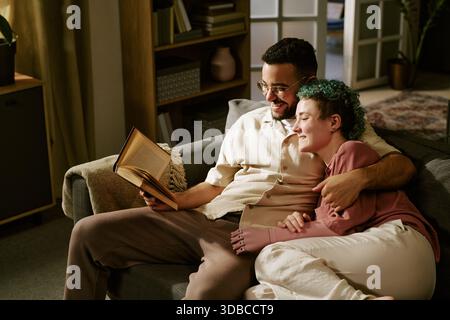 Young Woman e Young Man che si rilassano insieme leggendo Libro sul divano Foto Stock