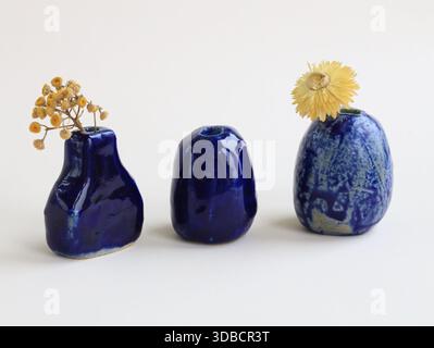 Studio minimalista Still Life con tre vasi in ceramica in miniatura fatti a mano con glassa blu e fiori secchi. Composizione pulita, scultorea Foto Stock