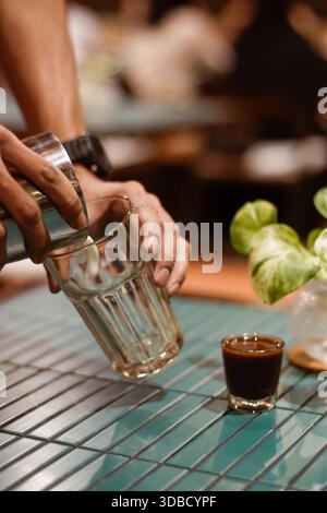 Il barista versa il latte montato nel bicchiere durante la preparazione del latte sul bancone del caffè, per chiudere il processo di preparazione del caffè Foto Stock