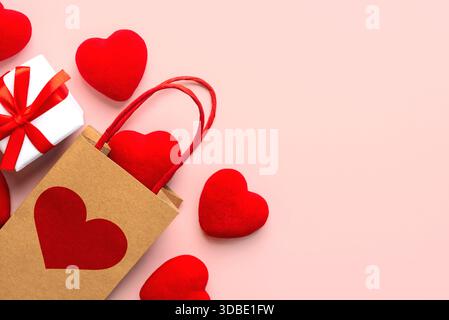 Vista dall'alto della shopping bag con cuore rosso, cuori rossi e spazio per testo su sfondo rosa. Concetto di San Valentino Foto Stock