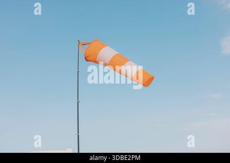 calza a vento a strisce arancioni e bianche che indica la direzione del vento su un palo contro un cielo blu limpido con nuvole leggere, concetto di monitoraggio meteorologico Foto Stock