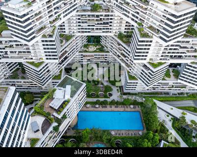 Vista aerea dei blocchi bianchi impilati dell'Interlace Condominium che contrastano con i lussureggianti cortili verdi e l'invitante piscina blu, Singa Foto Stock