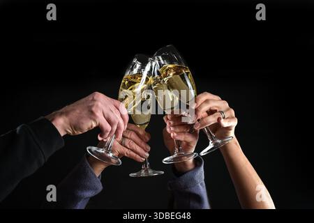 Brindisi a quattro mani con flute di champagne durante le feste di sera, per festeggiare Capodanno, Natale, compleanno o lavoro, sfondo scuro, Foto Stock