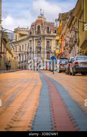 Veduta di una lunga strada con motivi di mattoni colorati che conduce ad un edificio dall'architettura ornata sotto un cielo nuvoloso, Quito, Ecuador. Foto Stock
