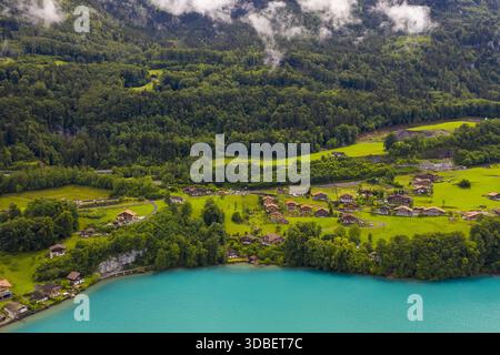 Vista aerea delle acque turchesi che incontrano lussureggianti foreste verdi e pittoreschi tetti in una splendida mostra di bellezze naturali, Iseltwald, Canton Berna, Switze Foto Stock