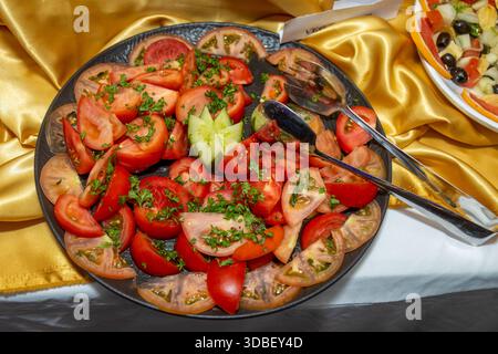 Insalata di pomodoro a fette fresche con prezzemolo e cetriolo guarnire su un piatto scuro Foto Stock