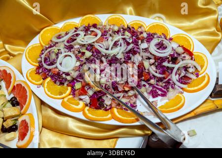 Insalata tritata colorata con cavolo rosso, pomodori, cipolle e fette d'arancia su un piatto Foto Stock